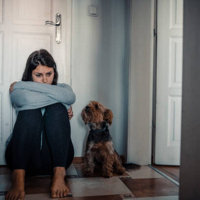 Woman with mental health problems is sitting desperate on the floor and  crying and her dog is next to her